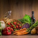 Arrangement of fresh vegetables and fruits on a wooden table with kitchen essentials.